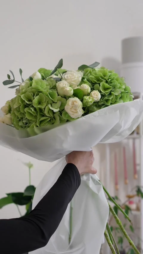 A florist adjusts the white packaging on a white and green bouquet of roses, hyd Stock Footage 317961653