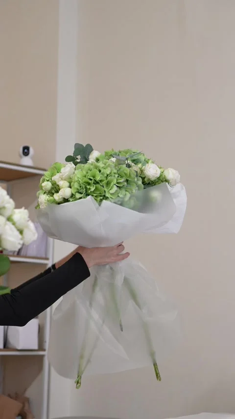 A florist adjusts the white packaging on a white and green bouquet of roses, hyd Stock Footage 317961663