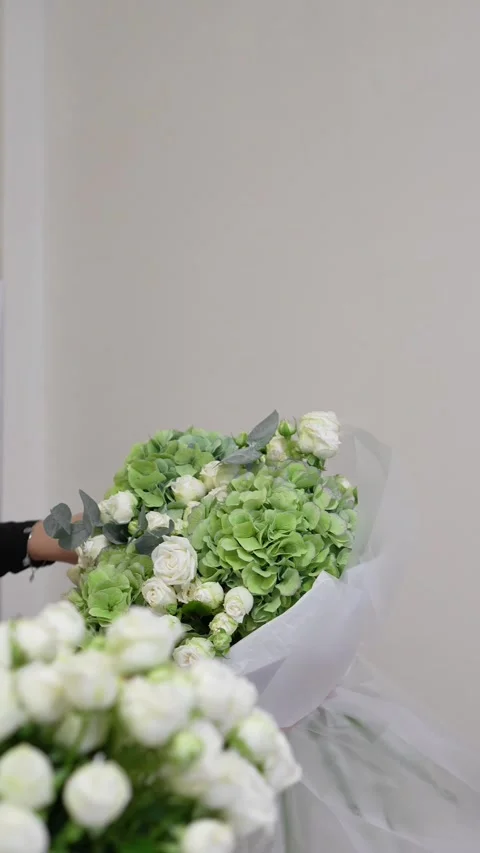 A florist adjusts the white packaging on a white and green bouquet of roses, hyd Stock Footage 317961674
