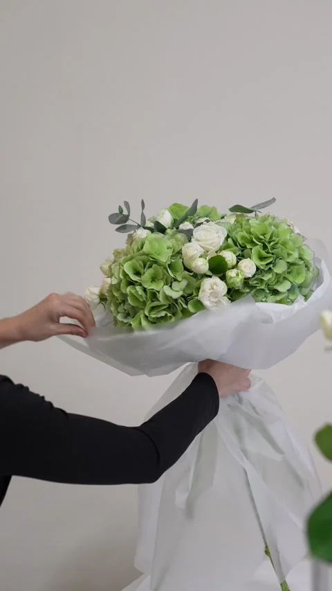 A florist adjusts the white packaging on a white and green bouquet of roses, hyd Stock Footage 317961678