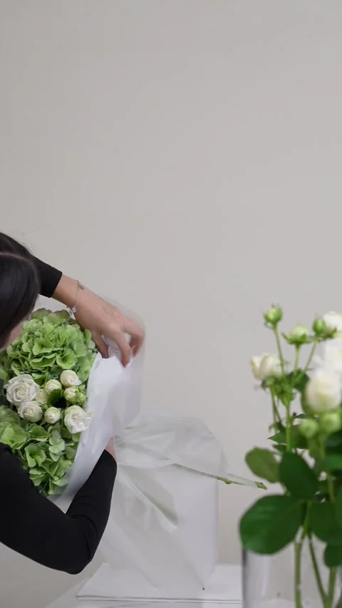 A florist adjusts the white packaging on a white and green bouquet of roses, hyd Stock Footage 317961691