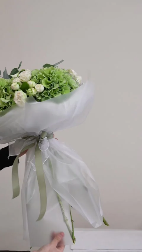 A florist adjusts the white packaging on a white and green bouquet of roses, hyd Stock Footage 317961709