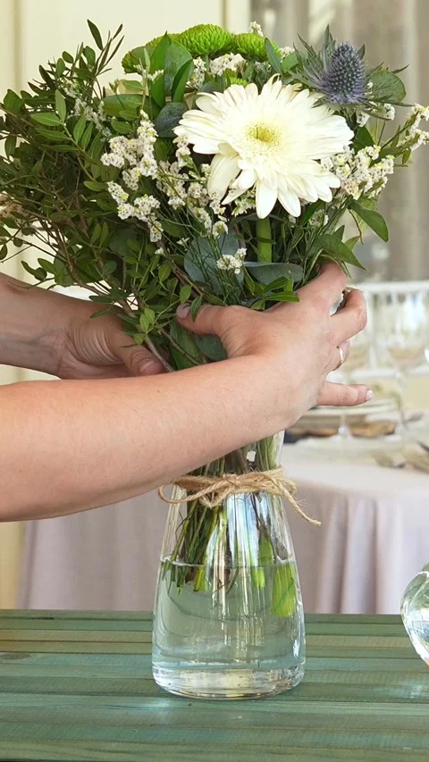 Florist carefully arranging pristine white, verdant green stems in glass vase Video stock 311012931