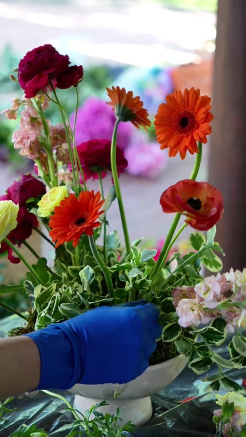Florist inserts orange ranunculus into a colorful wedding ekibana in a vase. wed Stock Footage 318558076