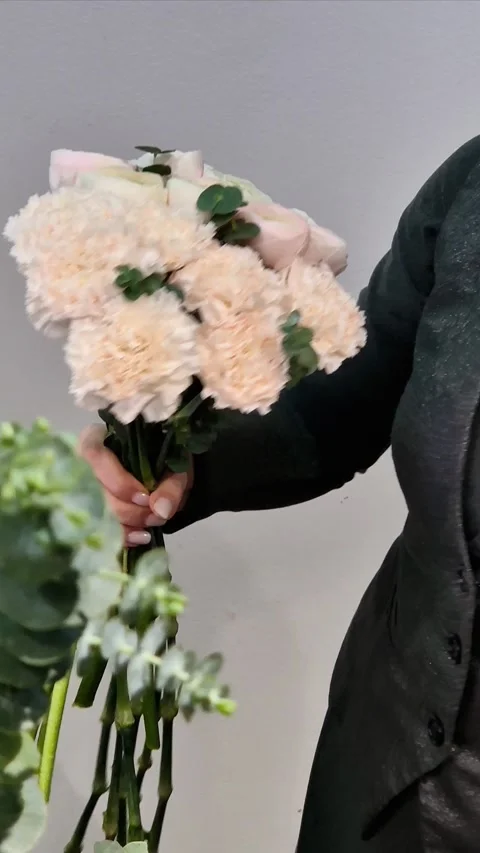 A florist makes a bouquet to order from carnations, ranunculus, and eucalyptu Stock Footage 302254487