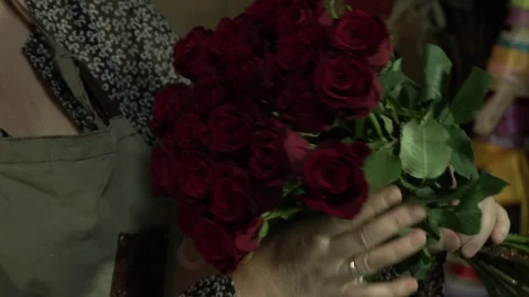The florist processes and makes a bouquet of scarlet red maroon roses Stock Footage 123684935