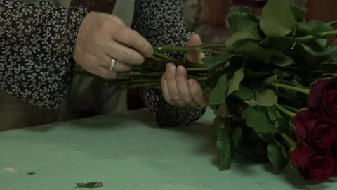 The florist processes and makes a bouquet of scarlet red maroon roses Stock Footage 123684940