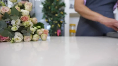 Florist rolls a paper on the table to wrap bouquet of roses, closeup view. Stock Footage 112654836