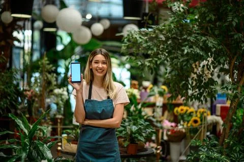 Florist showing a smartphone while surrounded with flowers and plants in a fl Stock Photos