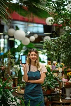 Florist showing a smartphone while surrounded with flowers and plants in a fl Stock Photos