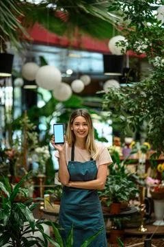 Florist showing a smartphone while surrounded with flowers and plants in a fl Stock Photos