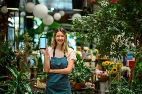 Florist showing a smartphone while surrounded with flowers and plants in a fl Stock Photos