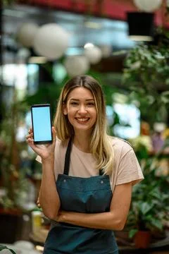 Florist showing a smartphone while surrounded with flowers and plants in a fl Stock Photos