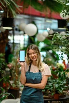 Florist showing a smartphone while surrounded with flowers and plants in a fl Stock Photos