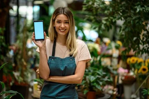 Florist showing a smartphone while surrounded with flowers and plants in a fl Stock Photos