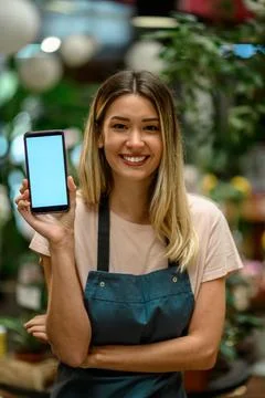 Florist showing a smartphone while surrounded with flowers and plants in a fl Stock Photos