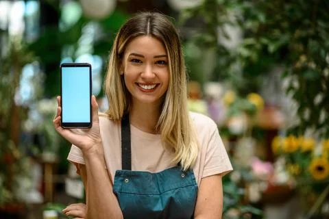 Florist showing a smartphone while surrounded with flowers and plants in a fl Stock Photos