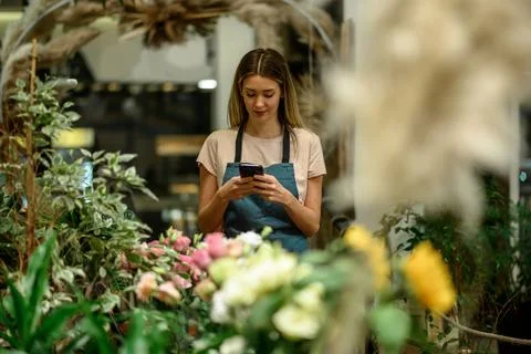 Florist using smartphone while surrounded with flowers and plants in a flower Stock Photos