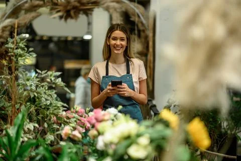 Florist using smartphone while surrounded with flowers and plants in a flower Stock Photos