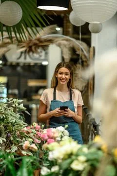 Florist using smartphone while surrounded with flowers and plants in a flower Stock Photos