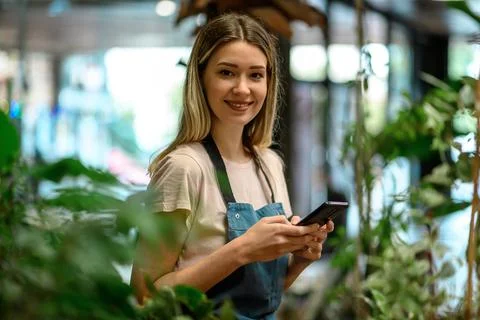 Florist using smartphone while surrounded with flowers and plants in a flower Stock Photos
