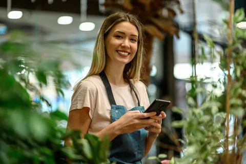 Florist using smartphone while surrounded with flowers and plants in a flower Stock Photos