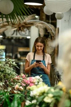 Florist using smartphone while surrounded with flowers and plants in a flower Stock Photos