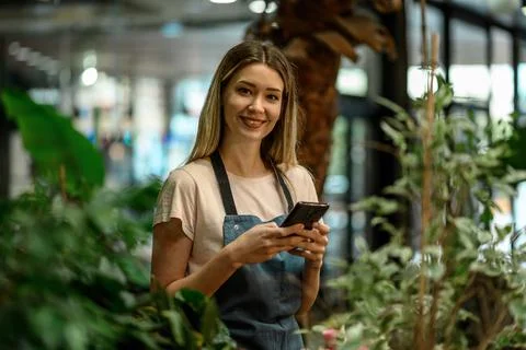 Florist using smartphone while surrounded with flowers and plants in a flower Stock Photos