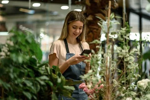 Florist using smartphone while surrounded with flowers and plants in a flower Stock Photos