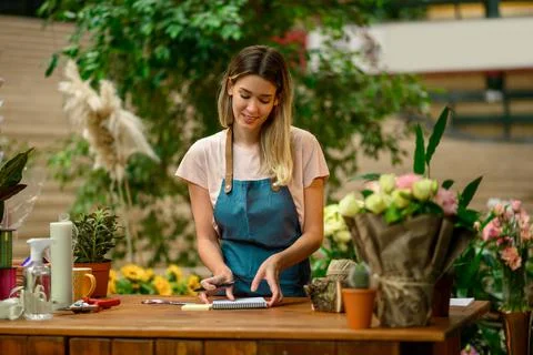 Florist writing in notebook while leaning against counter in a flower shop Stock Photos