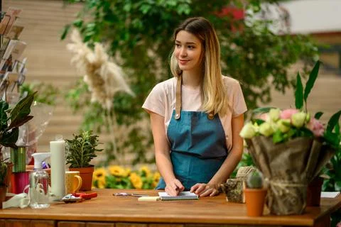 Florist writing in notebook while leaning against counter in a flower shop Stock Photos