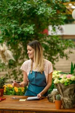 Florist writing in notebook while leaning against counter in a flower shop Stock Photos
