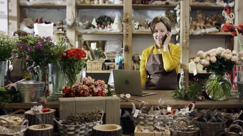 Florist in yellow blouse prints something on a laptop, and speking by the phone Stock Footage 101705290
