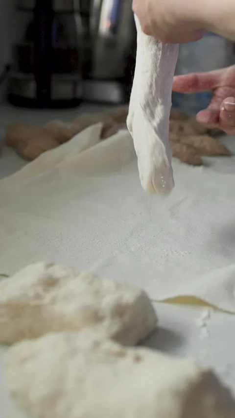 Flour-dusted hands shape and lift bread dough on parchment in soft kitchen Stock Footage 339306686