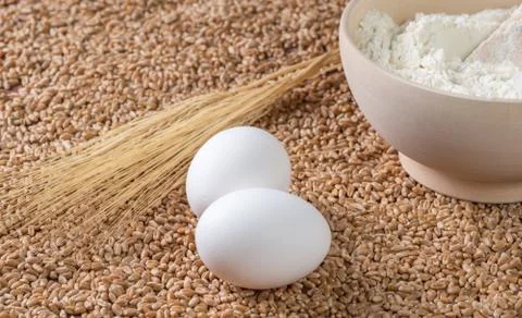 Flour, eggs, wheat ears on a background of grains. Stock Photos
