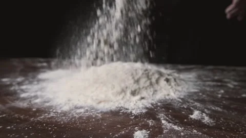 Flour is falling on the black table in slow motion. Someone throwing flour on a Stock-Footage 131237720