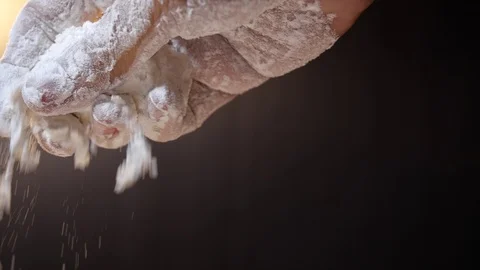 Flour falling from hand in slow motion on black background.  4K Stock Footage 124038100