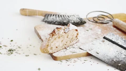 Flour falling onto slice of sourdough bread and baking tools on cutting board Stock Footage 195999212