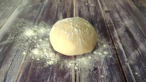 Flour falls on a round ball of dough on a wooden table Stock Footage 232219083