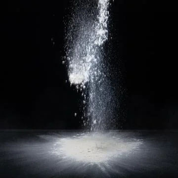 Flour falls on a table on a dark background . Stock Photos