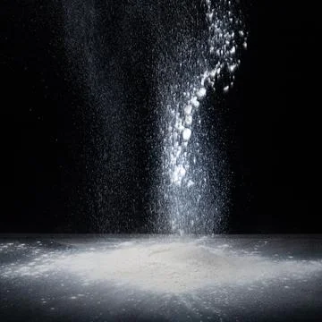 Flour falls on a table on a dark background . Stock Photos
