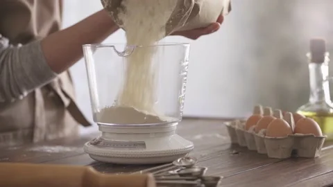 The flour in a paper bag falls into a transparent measuring bowl. Mechanical Stock Footage 155077902
