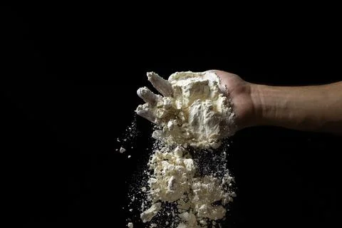 Flour is pouring from the hand on a black background. Stock Photos
