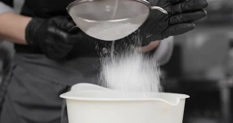 The flour is sieved through a sieve. Pastry chef's hands in black gloves Stock Footage 165578831