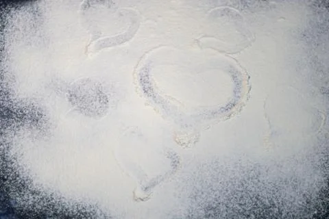 Flour is sprinkled on the table. They draw a heart on it with a finger. Valen Stock Photos