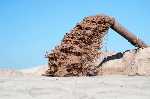 The flow of brown liquid from the pipe on the background of a pile of sand an Stock Photos