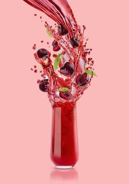Flow of red cherry juice flowing into drinking glass, flying cherry pieces, g Stock Photos
