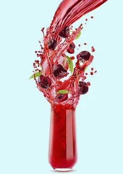 Flow of red cherry juice flowing into drinking glass, flying cherry pieces, g Stock Photos