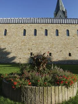 Flower bed in front of a stone wall with windows and a church tower in the Fotos de archivo