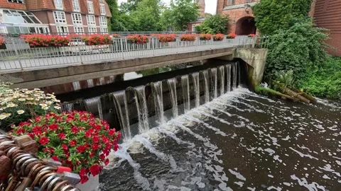 Flower Decorated Bridge Above Small Urban Weir and Flowing Water Stock Footage 340505641